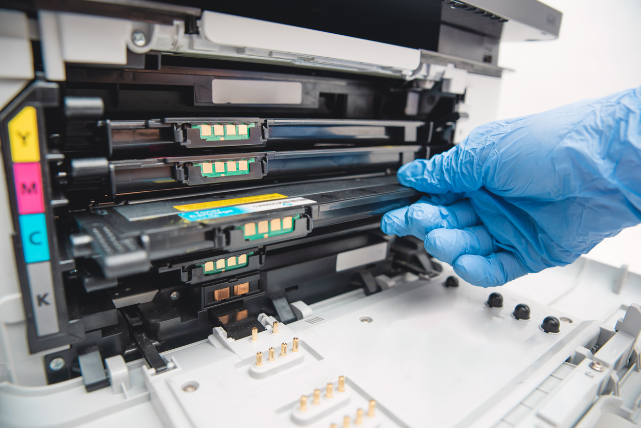 Man replacing toner in laser printer. Hand in gloves holding cyan toner.